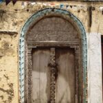 Ornate wooden door in a historical building with intricate carvings and textured facade.